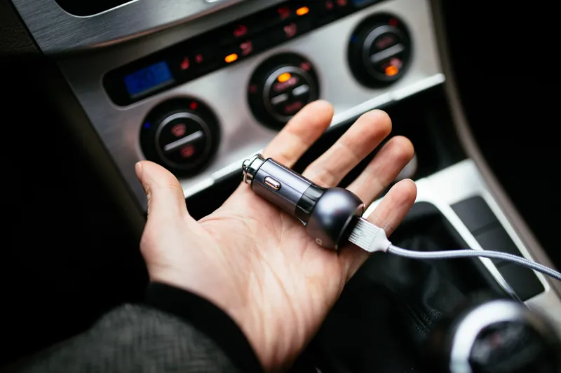 A hand holding a USB car charger in front of a 12V power outlet